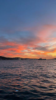 A vibrant sunset over a calm sea with a ferry sailing in the distance.
