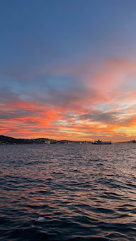 A vibrant sunset over a calm sea with a ferry sailing in the distance.