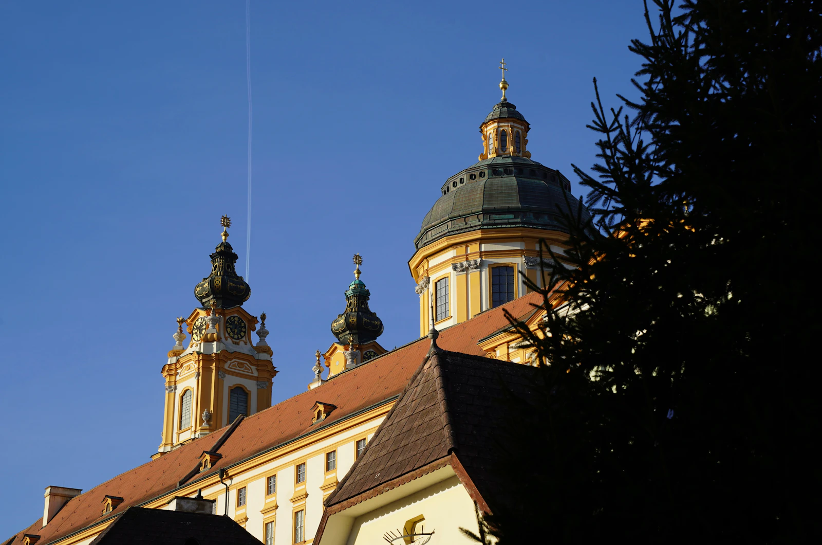 Travel photograph: The pale ochre façade and twin towers of Melk Abbey rising above trees.