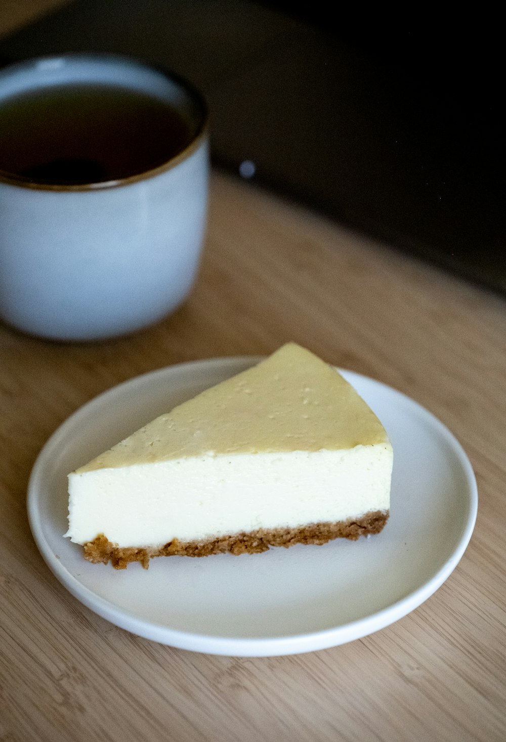 a piece of cheesecake on a plate next to a cup of tea