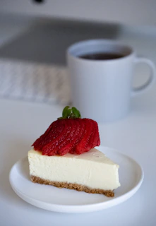 Close-up of a creamy cheesecake slice topped with fresh strawberries and mint leaves on a rustic wooden table