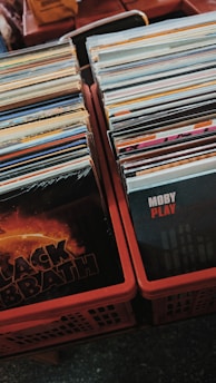 Stacks of vinyl records are neatly arranged in plastic crates. The front covers of two albums, one by Black Sabbath and another by Moby, are prominently visible, suggesting a collection of diverse music genres.