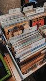 A collection of vinyl records organized in several rows, divided by labeled tabs indicating different music genres such as Rock, Jazz, and Funk, Soul. Visible album covers include artists like Ian Hunter and Stevie Wonder. The records are neatly arranged in a box with a wooden surface and some patterns partially visible on the left side.