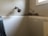 A bathroom corner displaying a shower head attached to the wall above a white bathtub. The upper corner of the wall appears to have mold or mildew growth, indicated by dark, discolored areas near the shower.
