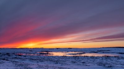 An expansive icy landscape with distant mountains and a vibrant sunset.