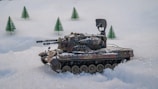 A model tank is positioned on a snowy landscape with miniature evergreen trees in the background. The tank features intricate details, including weaponry and camouflage paint.