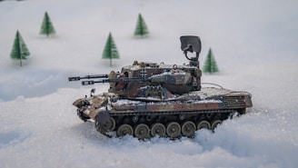 A model tank is positioned on a snowy landscape with miniature evergreen trees in the background. The tank features intricate details, including weaponry and camouflage paint.
