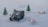 A miniature military vehicle is set on a snowy landscape, surrounded by small lit tealight candles and tiny model pine trees. The scene creates a winter diorama effect.