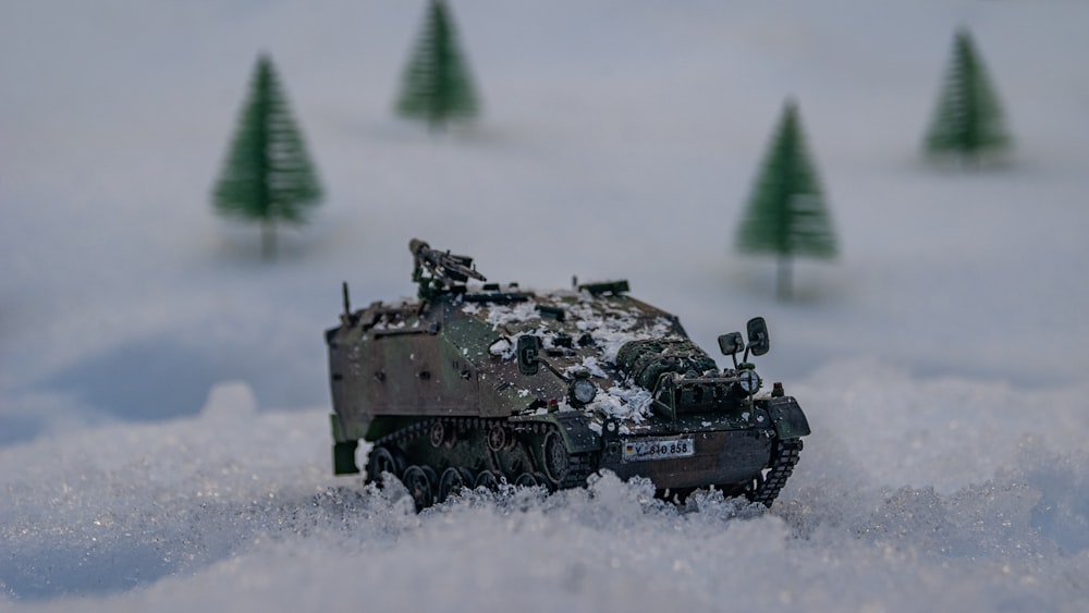 a toy army tank in the snow with trees in the background