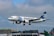 An airplane with white and blue colors is captured mid-air with its landing gear extended, flying against a cloudy sky. The aircraft has 'EGYPTAIR' written prominently on its fuselage, and it features a logo on the tail. In the background, an airport with various terminal buildings and other parked airplanes can be seen.