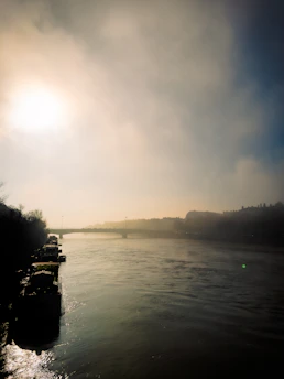 Sunrise over a misty river winding through an ancient village, with soft golden light illuminating worn wooden boats.