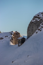 A sleek, modern prefabricated cottage nestled on a snowy mountain slope under a cloudy sky.