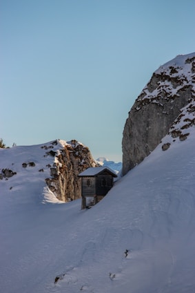 A sleek, modern prefabricated cottage nestled on a snowy mountain slope under a cloudy sky.