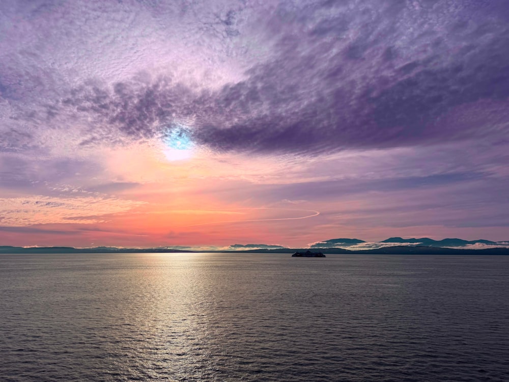 a beautiful sunset over the ocean with a boat in the distance