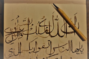 Close-up of hands writing Arabic calligraphy with a traditional pen on parchment.
