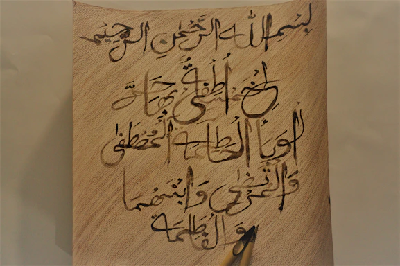 A textured parchment background with an elegant vintage Arabic calligraphy pen resting on it.