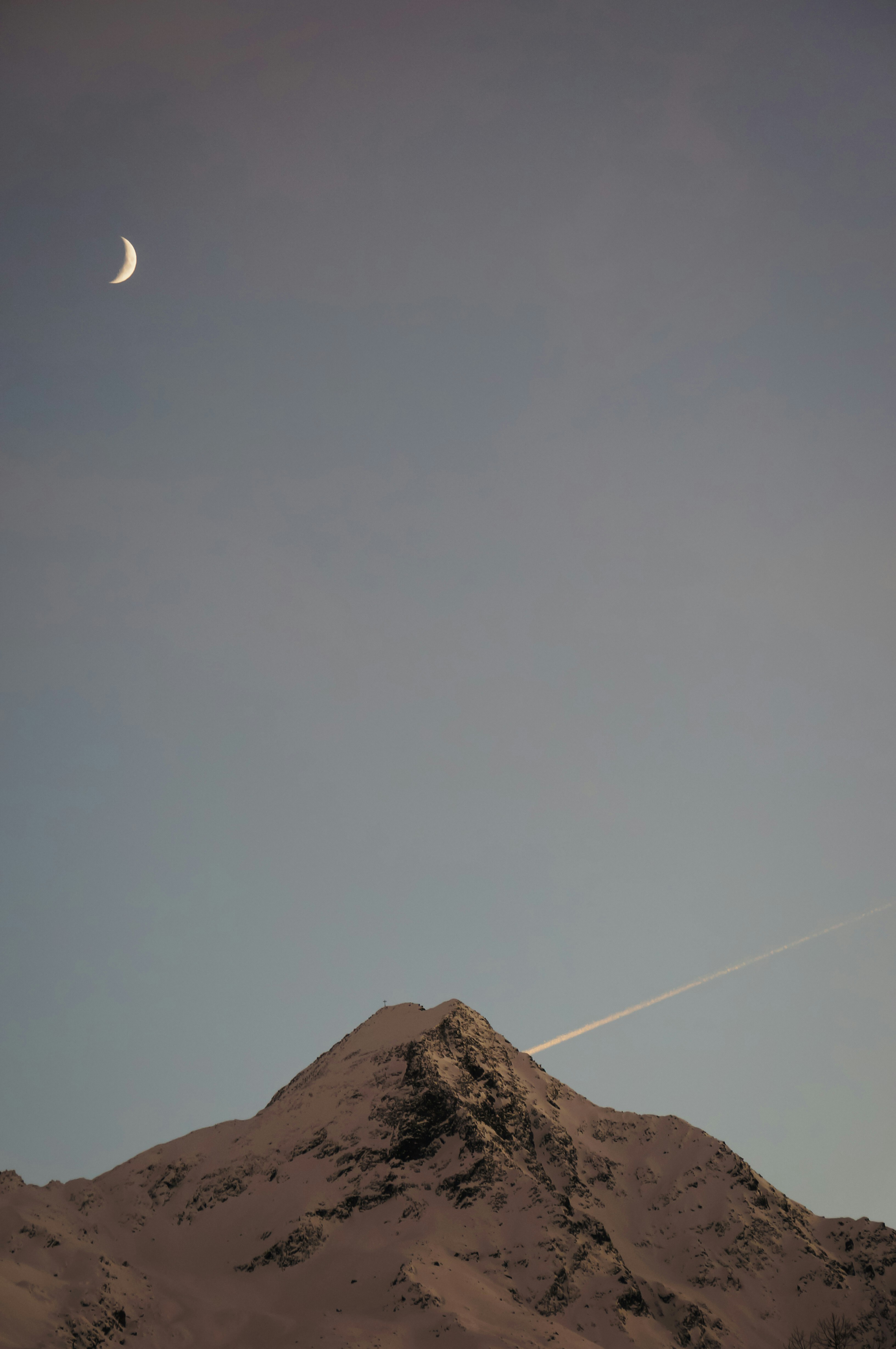 a plane flying over a mountain with a moon in the sky
