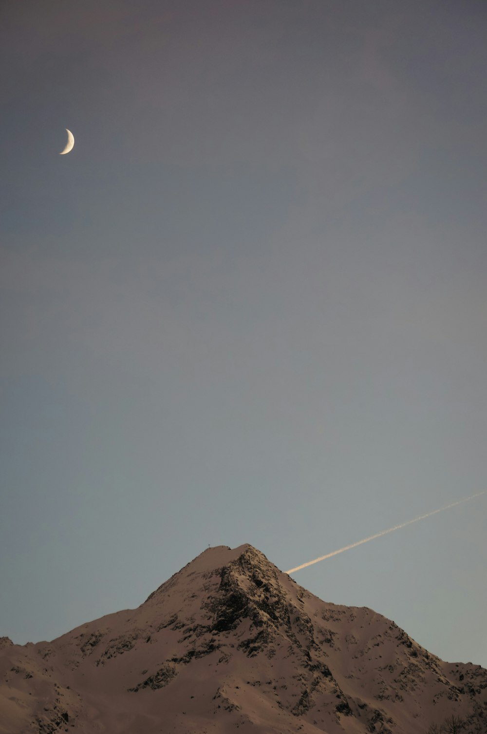 um avião sobrevoando uma montanha com uma lua no céu