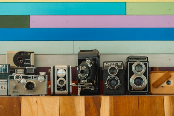 An array of colorful camera bodies displayed neatly on a minimalist white shelf.