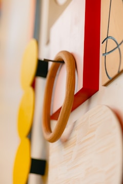 A close-up view of a modern, abstract wall design featuring geometric shapes. The composition includes wooden circles, a rectangular red frame, and a board with abstract linework. Earthy tones are prominent, contributing to a contemporary aesthetic.
