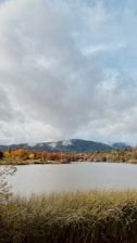 A serene lake surrounded by autumn-colored trees and distant mountain peaks.