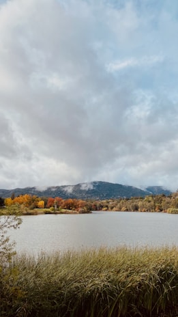 A serene lake surrounded by autumn-colored trees and distant mountain peaks.