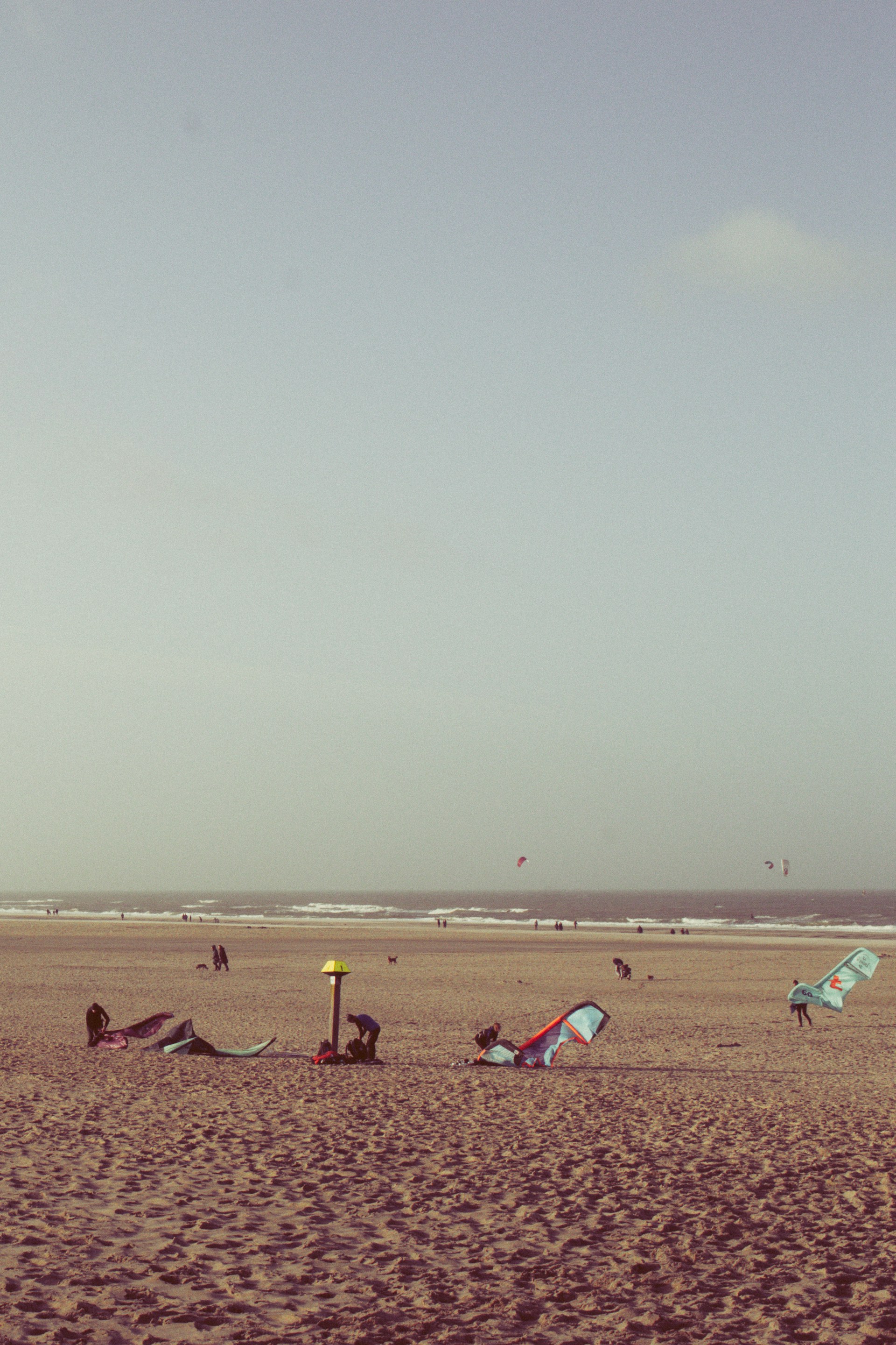 A group of friends setting up their kiteboarding gear on a sandy beach.