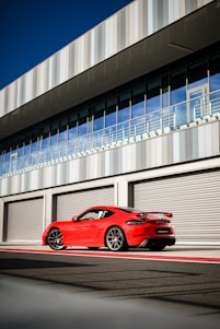 A sleek red and black GT Cars rental vehicle parked in front of a modern office building.