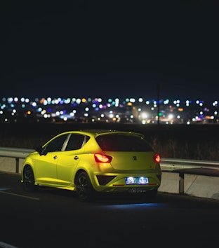 A bright yellow tow truck assisting a stranded car on a dark asphalt road at dusk
