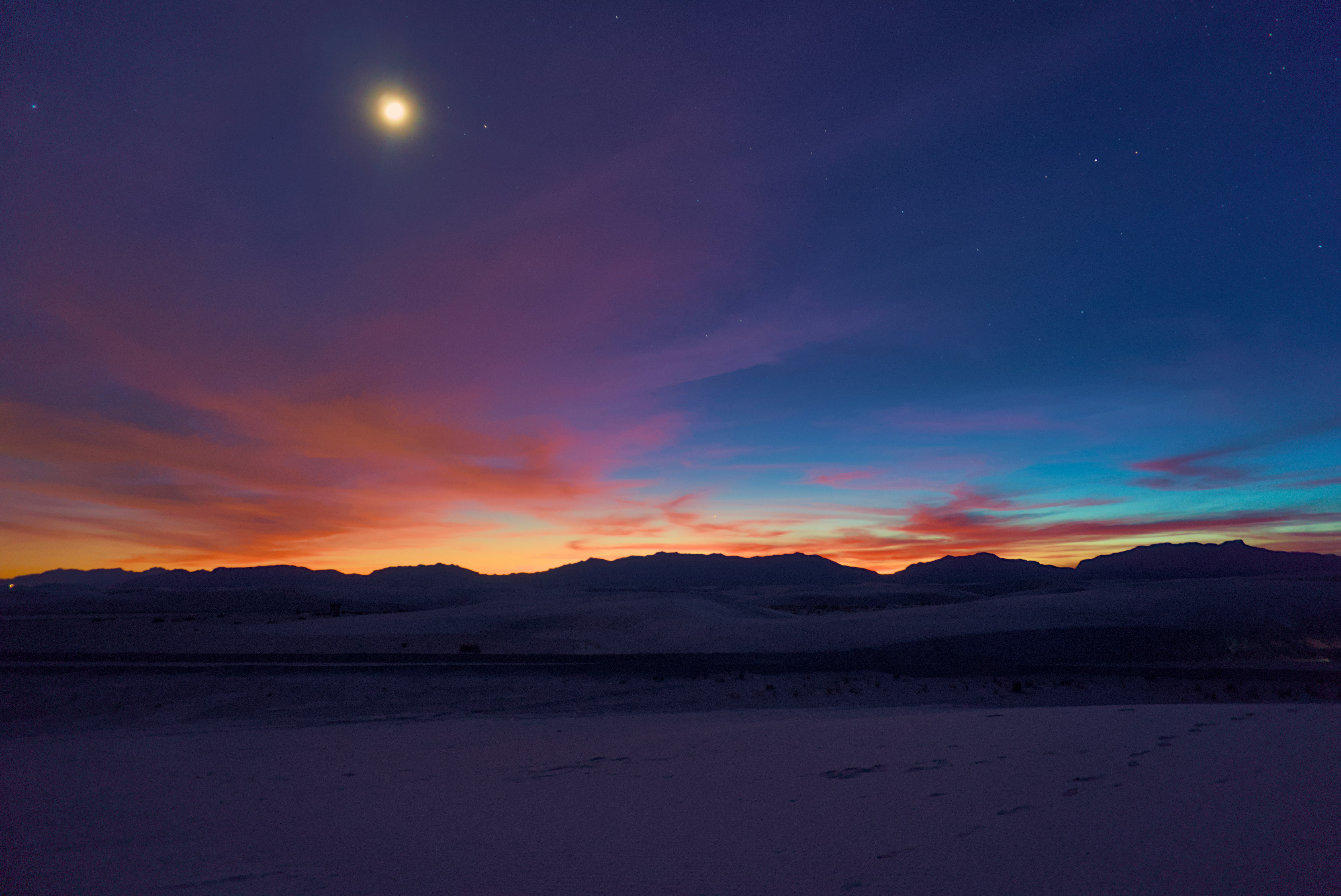 the moon is setting over the mountains in the distance, 