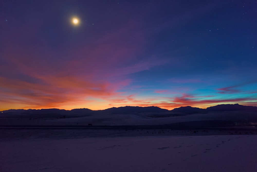 the moon is setting over the mountains in the distance