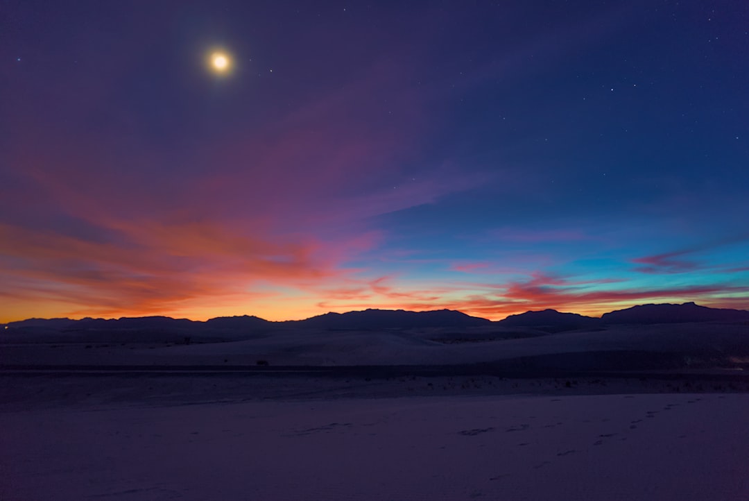 the moon is setting over the mountains in the distance,