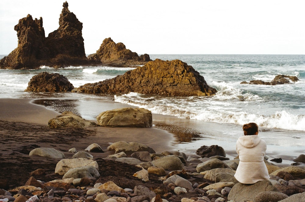 a woman standing on a rocky beach next to the ocean