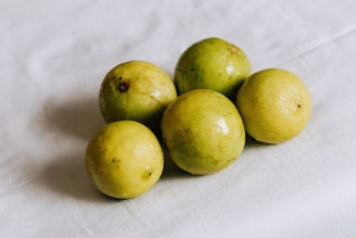 Five round, slightly mottled yellow-green fruits are arranged on a white cloth surface, displaying a glossy and fresh appearance.