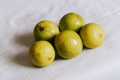 Five round, slightly mottled yellow-green fruits are arranged on a white cloth surface, displaying a glossy and fresh appearance.