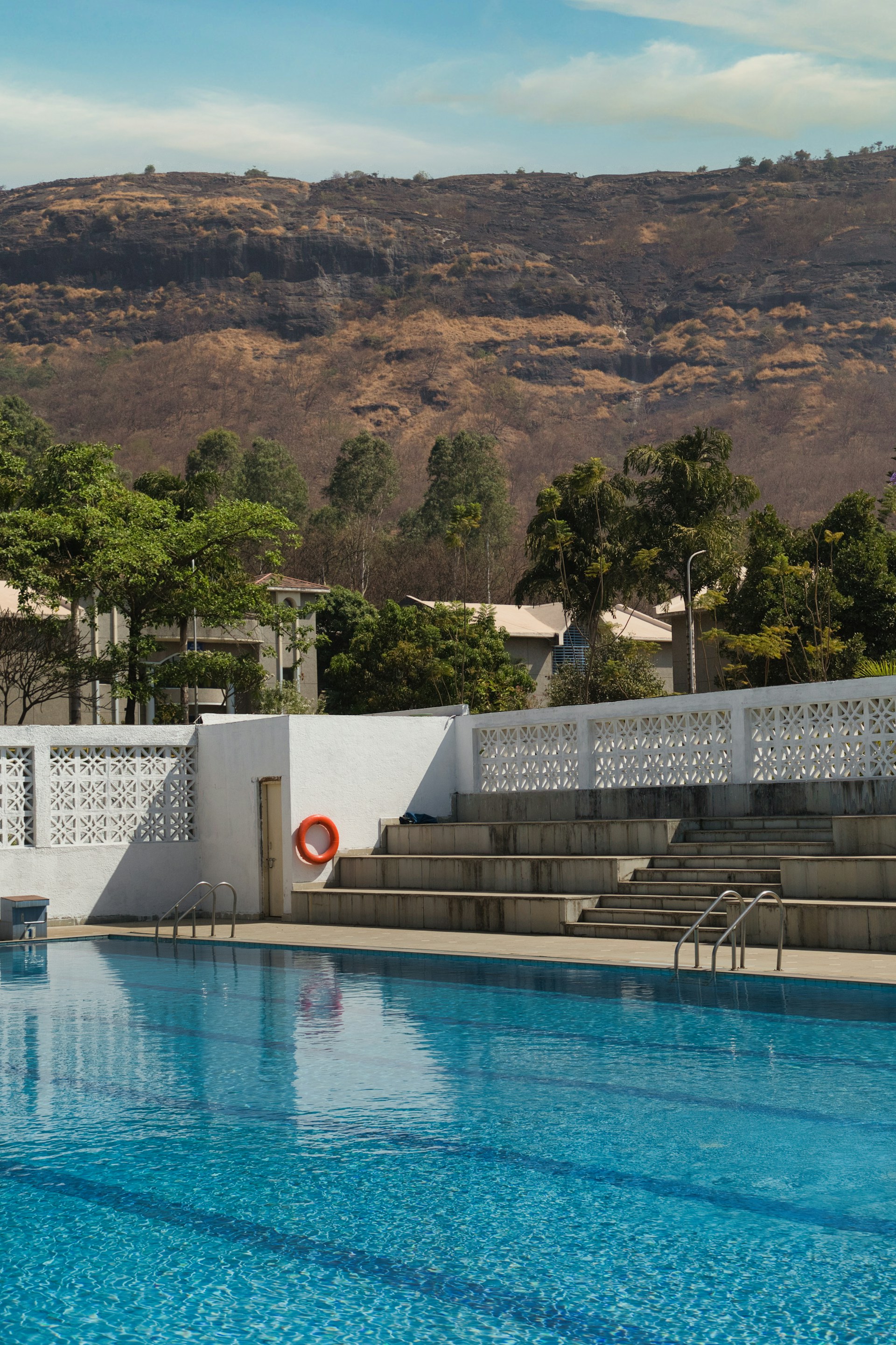 Inviting swimming pool surrounded by minimalist stone walls and lush greenery under a clear blue sky.