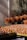 Numerous brown eggs are displayed in orange baskets and large woven trays, with the eggs arranged in a market setting. The background includes a textured wall and fishing nets draped above the baskets, suggesting a rustic or artisanal environment.