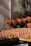 Numerous brown eggs are displayed in orange baskets and large woven trays, with the eggs arranged in a market setting. The background includes a textured wall and fishing nets draped above the baskets, suggesting a rustic or artisanal environment.