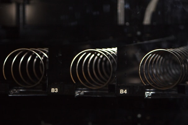 Coils of a vending machine in an empty, dimly lit setting are visible. The spirals are metallic and shiny, placed in separate compartments labeled B3 and B4.