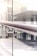 A close-up view of a modern railing in a building, with a sleek stainless steel design and glass panels. The background appears to be an office or a public space with tables and chairs.