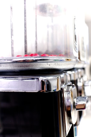 A close-up view of a metallic cylindrical appliance with a transparent section at the top containing small red objects. The appliance has a shiny, reflective metal surface with a knob on the side, suggesting it might be used for cooking or processing food.