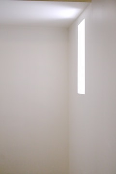 A minimalist white room with soft natural light streaming through large windows.