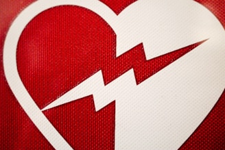 A white heart shape with a zigzag line splitting it in half is placed against a textured red background.
