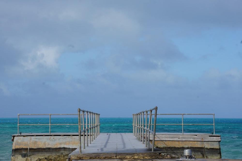 a wooden pier with a metal railing over the ocean