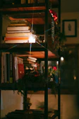 Moody bookshelf lined with fantasy and romance novels, illuminated by soft cream candlelight in a cozy nook.