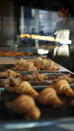A smiling baker holding a tray of golden croissants against a backdrop of pastel-colored walls.