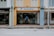 A man is entering a laundry shop with a signboard reading 'Laundry Team' above the entrance. The facade of the building features a mix of yellow and blue tones with adjacent storefronts visible on either side.