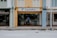 A man is entering a laundry shop with a signboard reading 'Laundry Team' above the entrance. The facade of the building features a mix of yellow and blue tones with adjacent storefronts visible on either side.