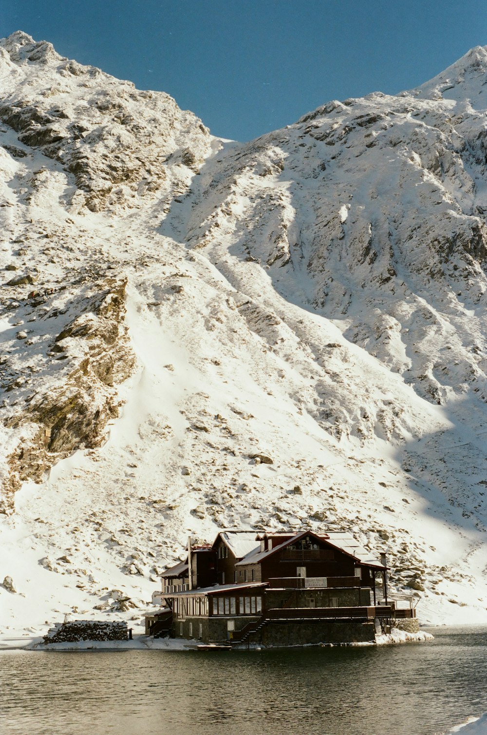 a house sitting on top of a lake in front of a snow covered mountain