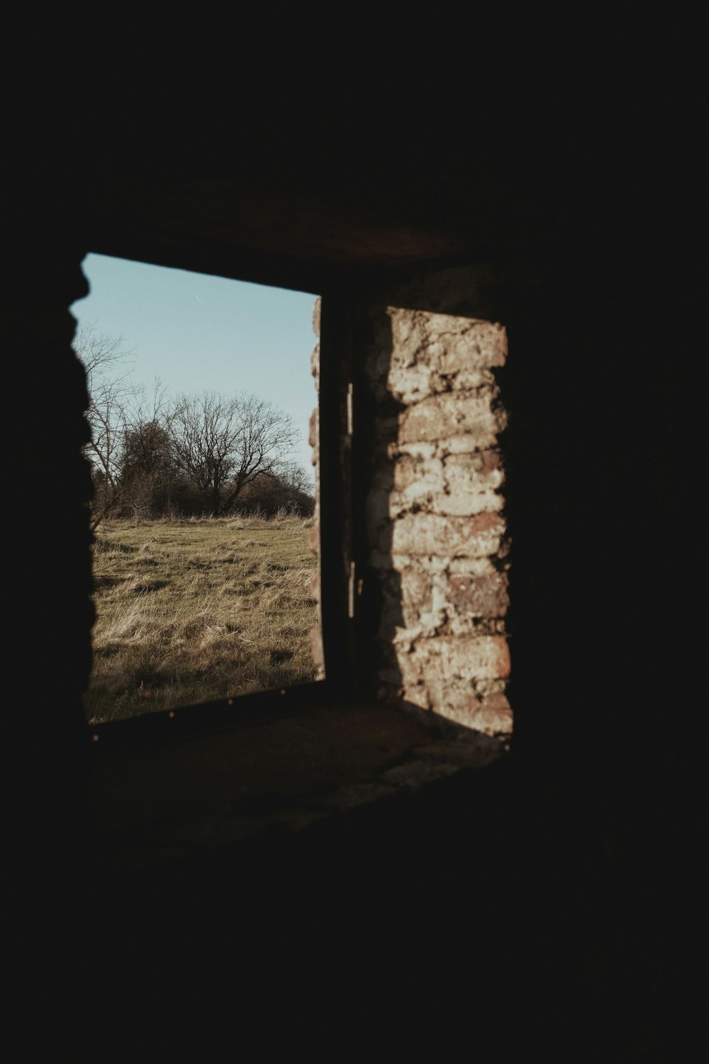 an open window in a stone building with a field in the background